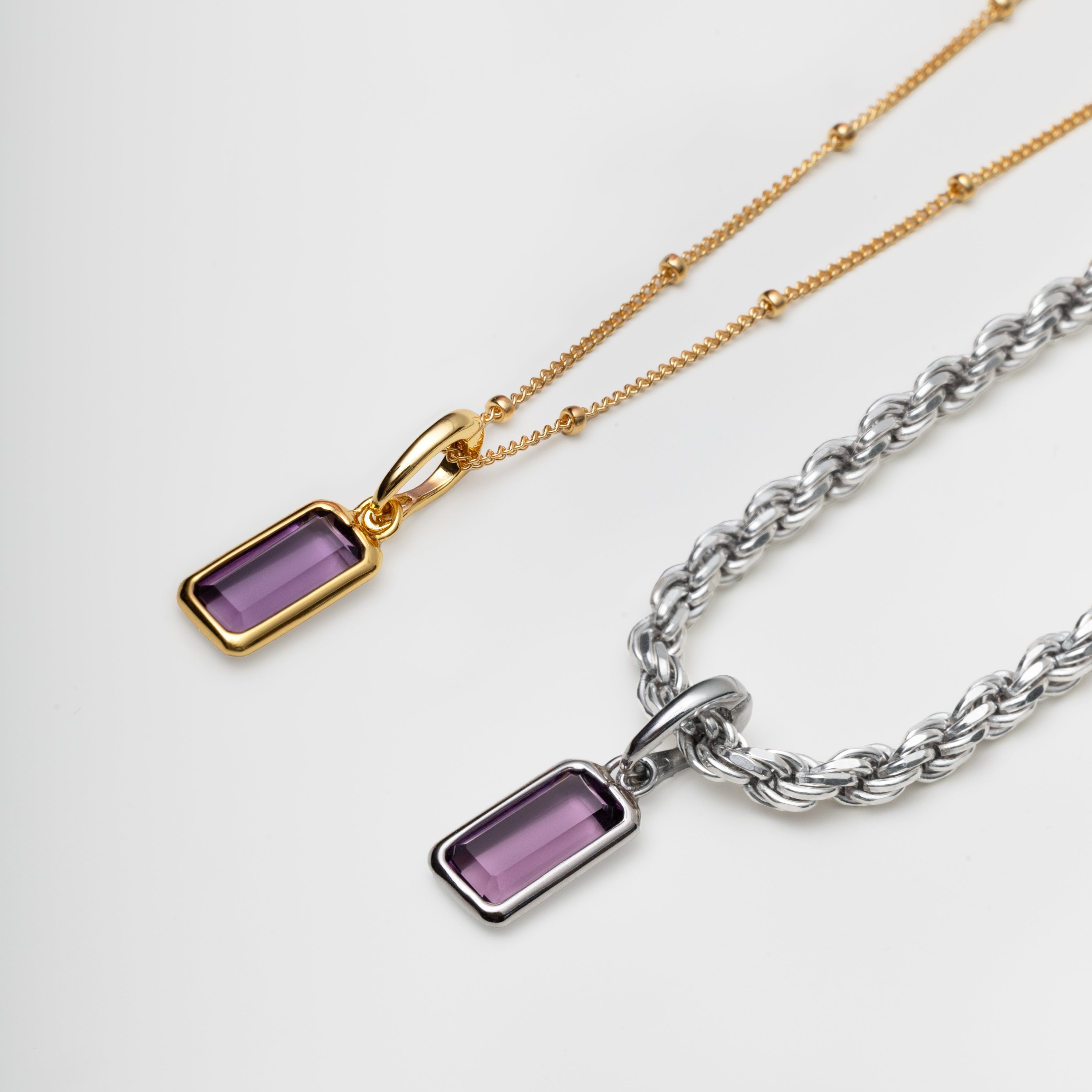 Two necklaces with amethyst purple gemstone pendants on gold and silver chains against a white background