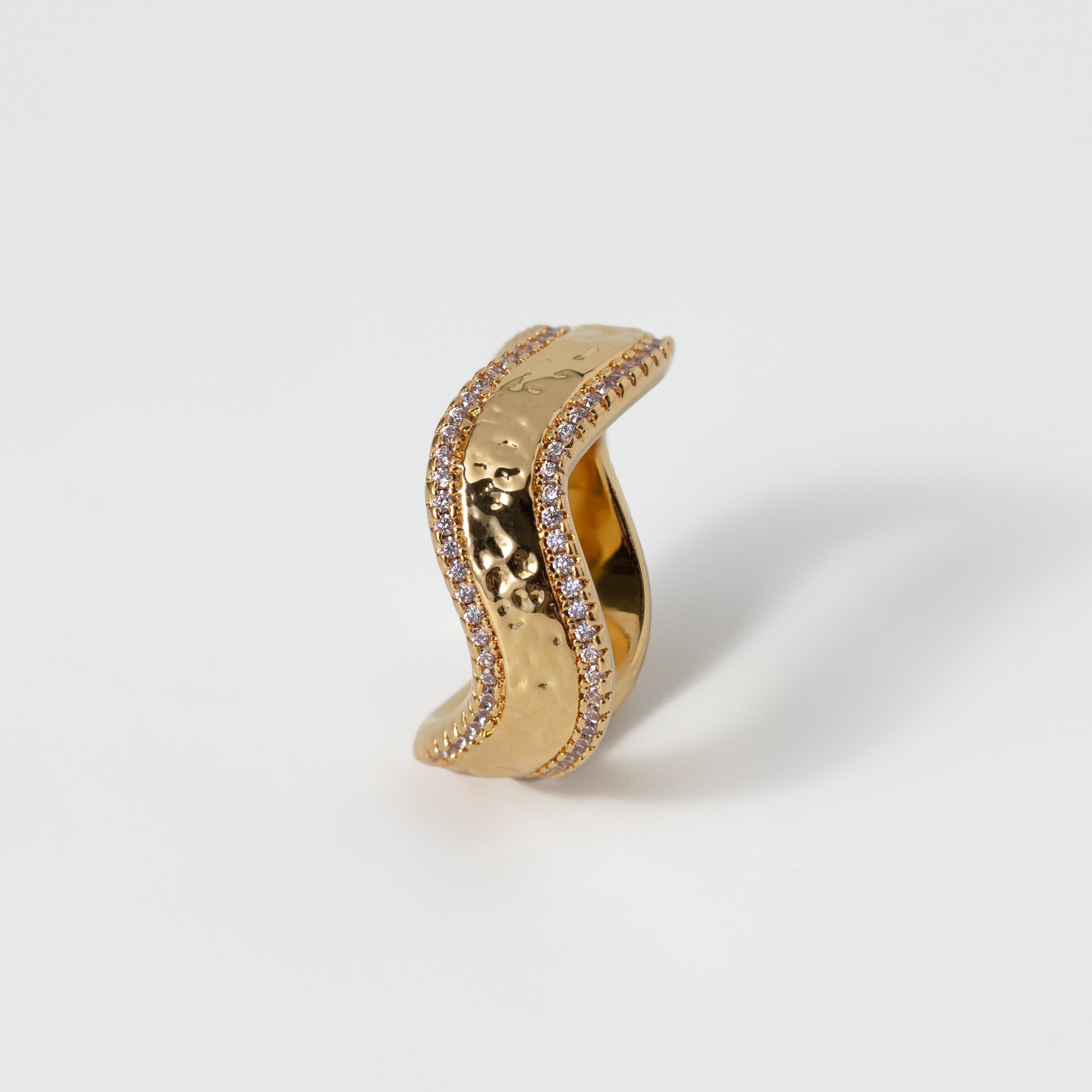 Gold ring with wavy design and small stones on a light gray background