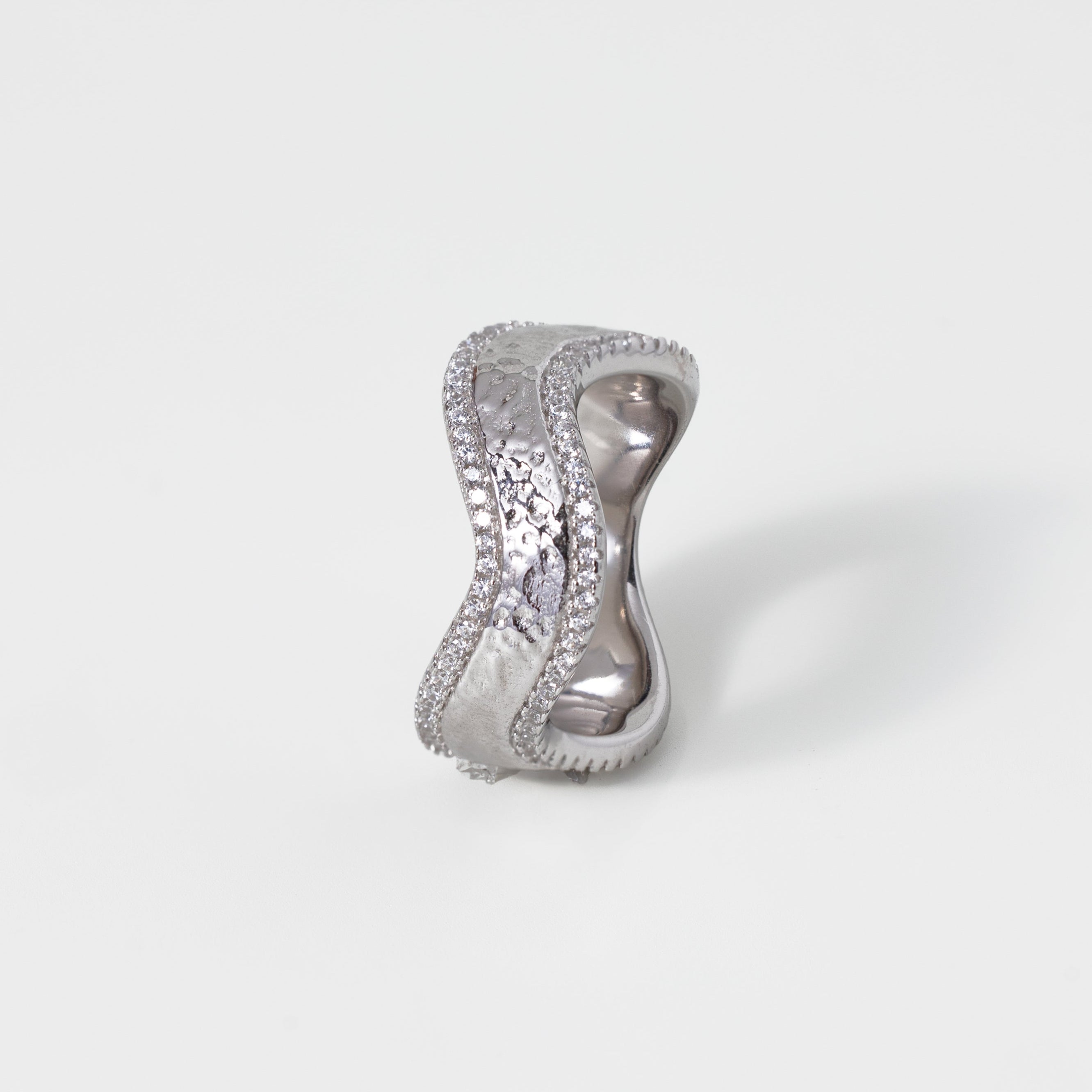 Silver ring with wavy diamond accents on a light gray background