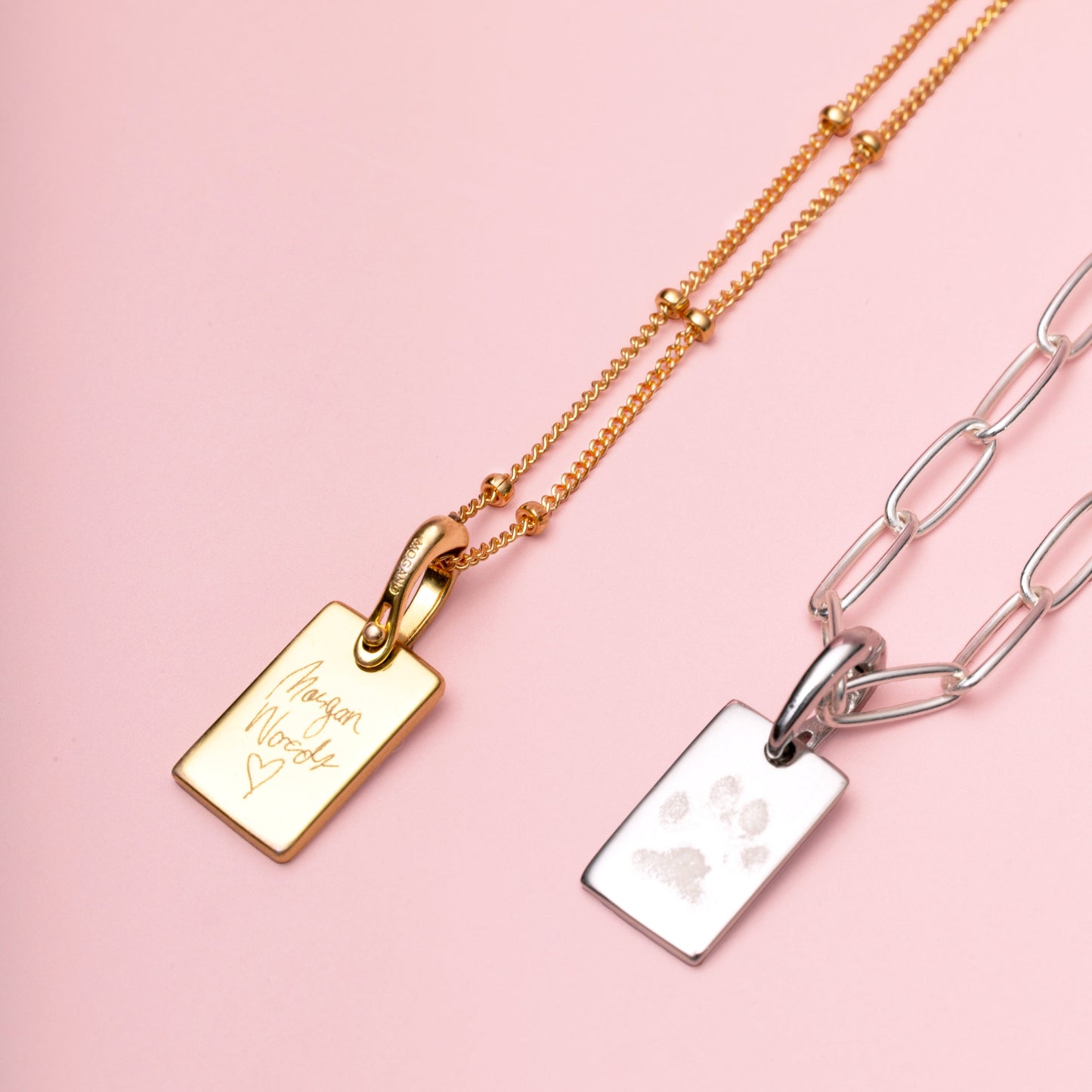 Two gold and silver necklaces with engraved tags on a pink background