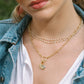 Close-up of a person wearing a gold necklace with a lock charm, pearl necklace, and denim jacket.