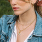 Woman wearing a denim jacket, pearl necklace, and gold earrings with a blurred green background