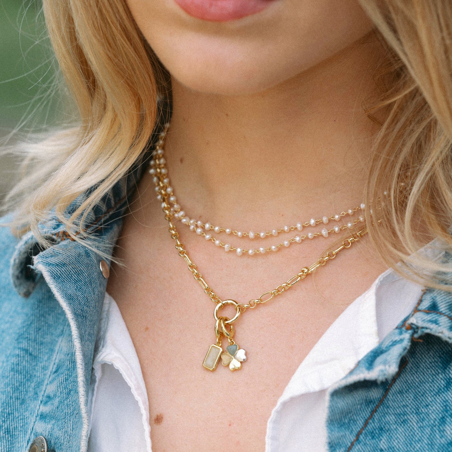 Close-up of a person wearing layered necklaces with a denim jacket and white shirt.