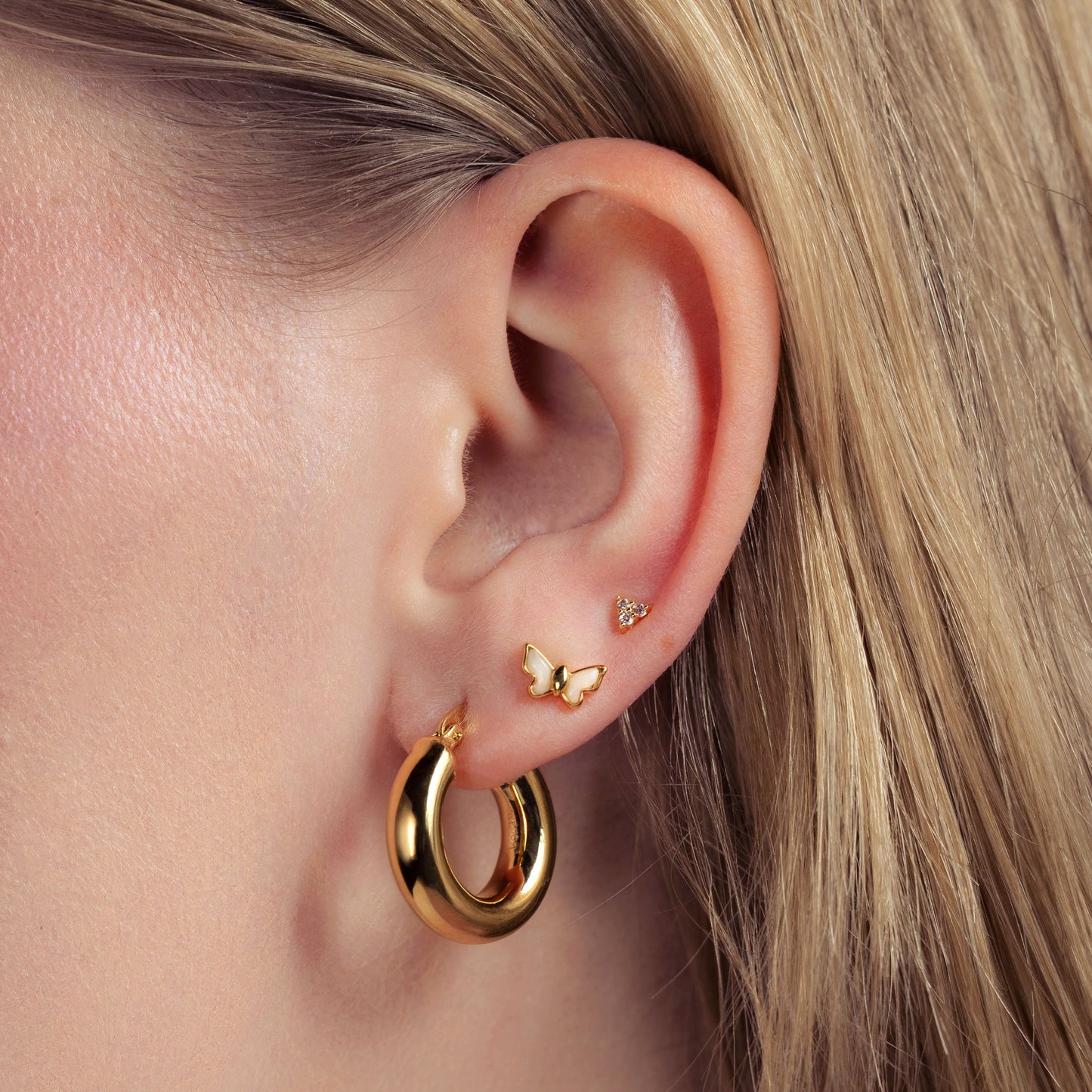 Close-up of an ear wearing gold hoop earrings with a butterfly accent.