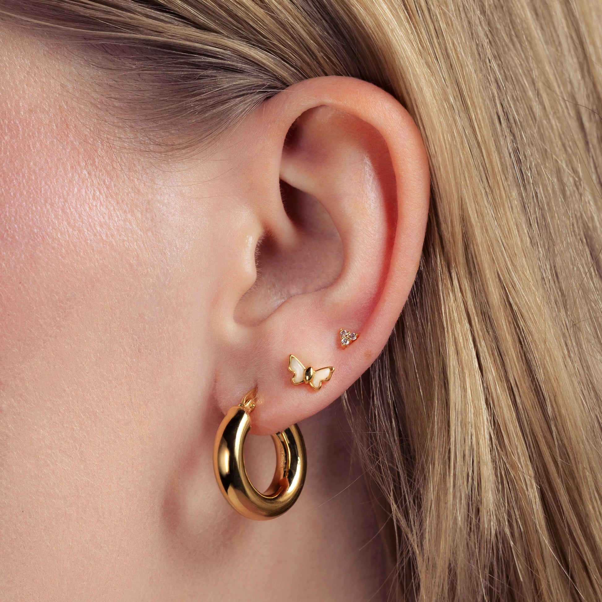 Close-up of an ear wearing gold hoop earrings with a butterfly accent.
