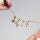 Gold necklace with various charms held by a hand against a gray background