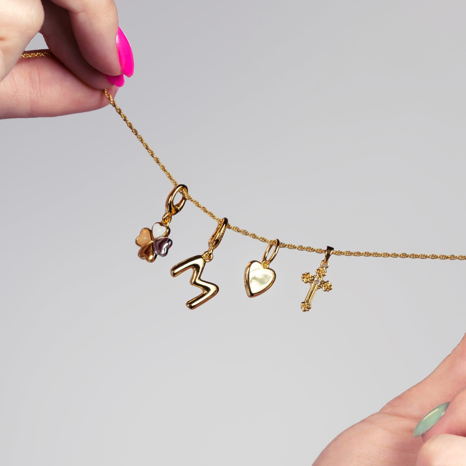 Gold necklace with various charms held by a hand against a gray background