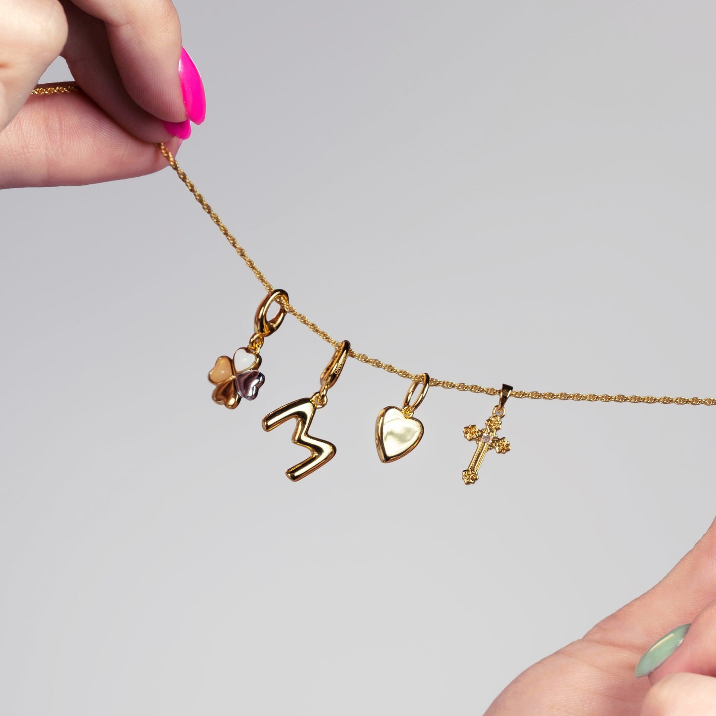 Gold necklace with various charms held by a hand against a gray background