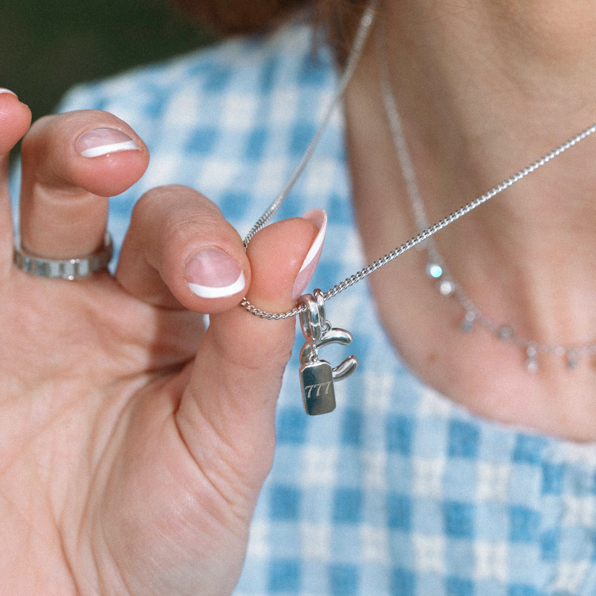 Close-up of a hand holding a necklace with a pendant, blurred background