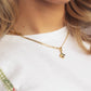 Close-up of a person wearing a gold necklace with a clover pendant, against a white background.