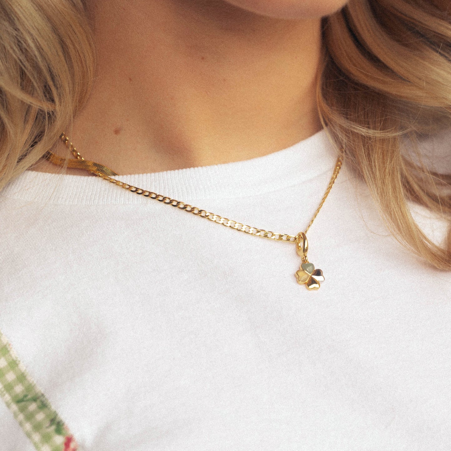 Close-up of a person wearing a gold necklace with a clover pendant, against a white background.