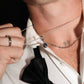 Close-up of a person wearing a white shirt with a black bow tie and multiple necklaces.