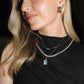 Woman wearing a black top and multiple necklaces with a dark background