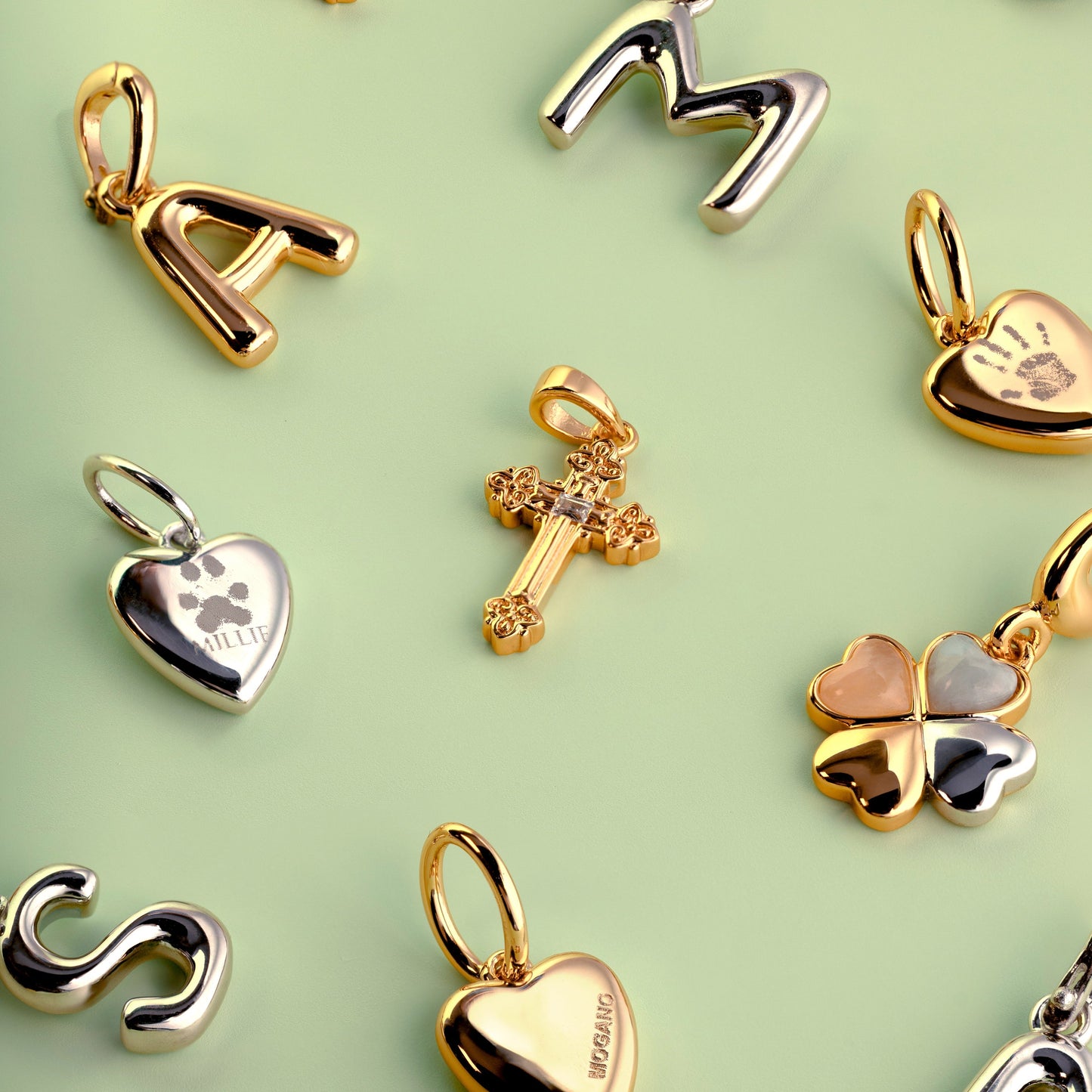 Gold pendants including letters, hearts, and crosses on a light green background