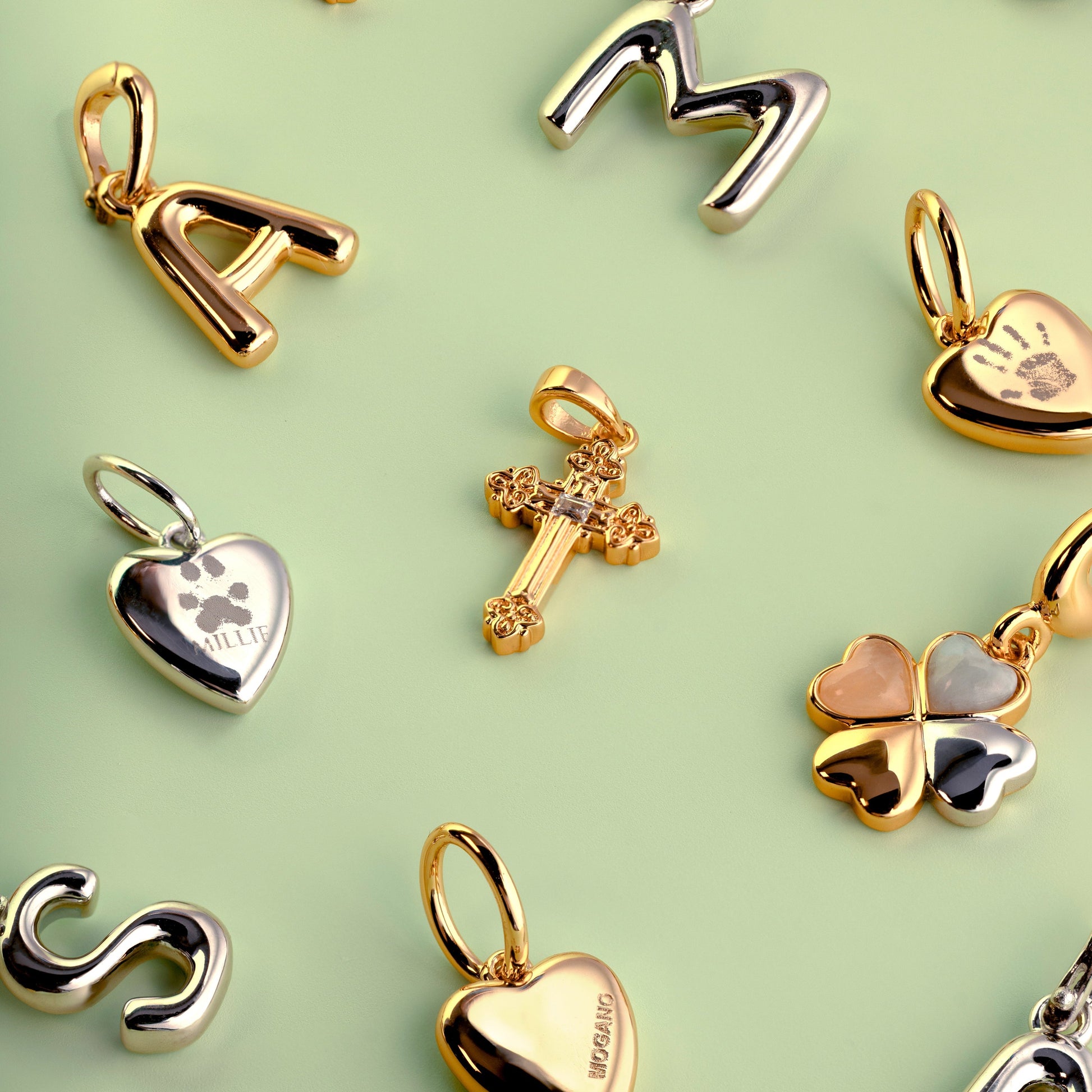 Gold pendants including letters, hearts, and crosses on a light green background