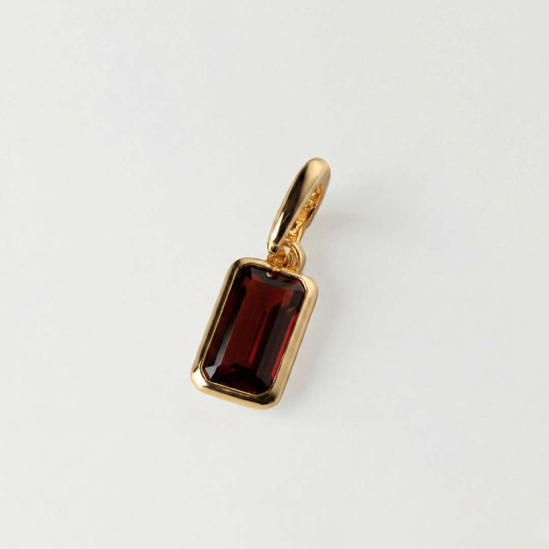Gold pendant with a red gemstone on a light gray background