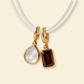 Two gold pendants with gemstones on a white cord against a beige background