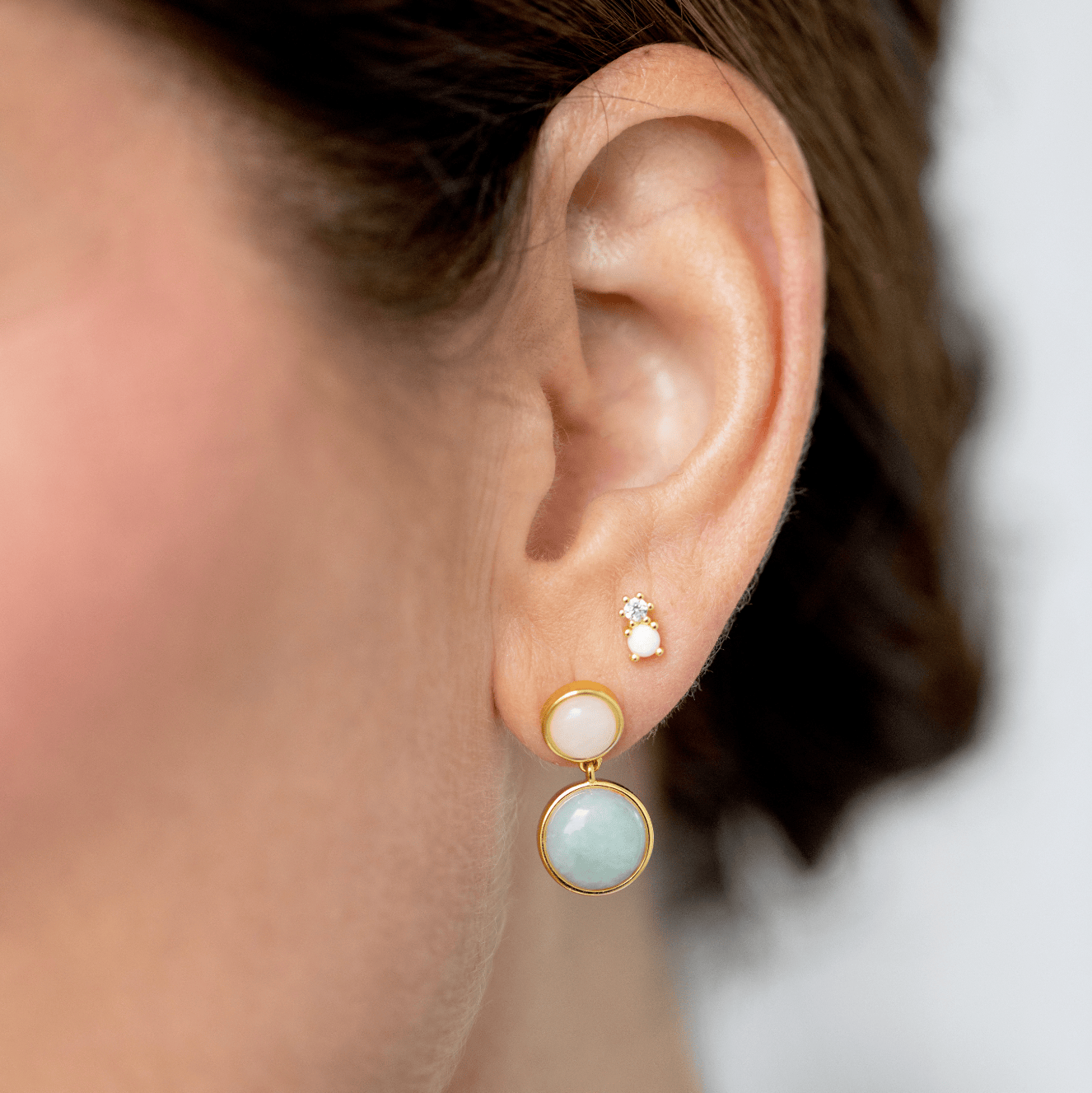 Close-up of an ear wearing gold earrings with opal gemstones.