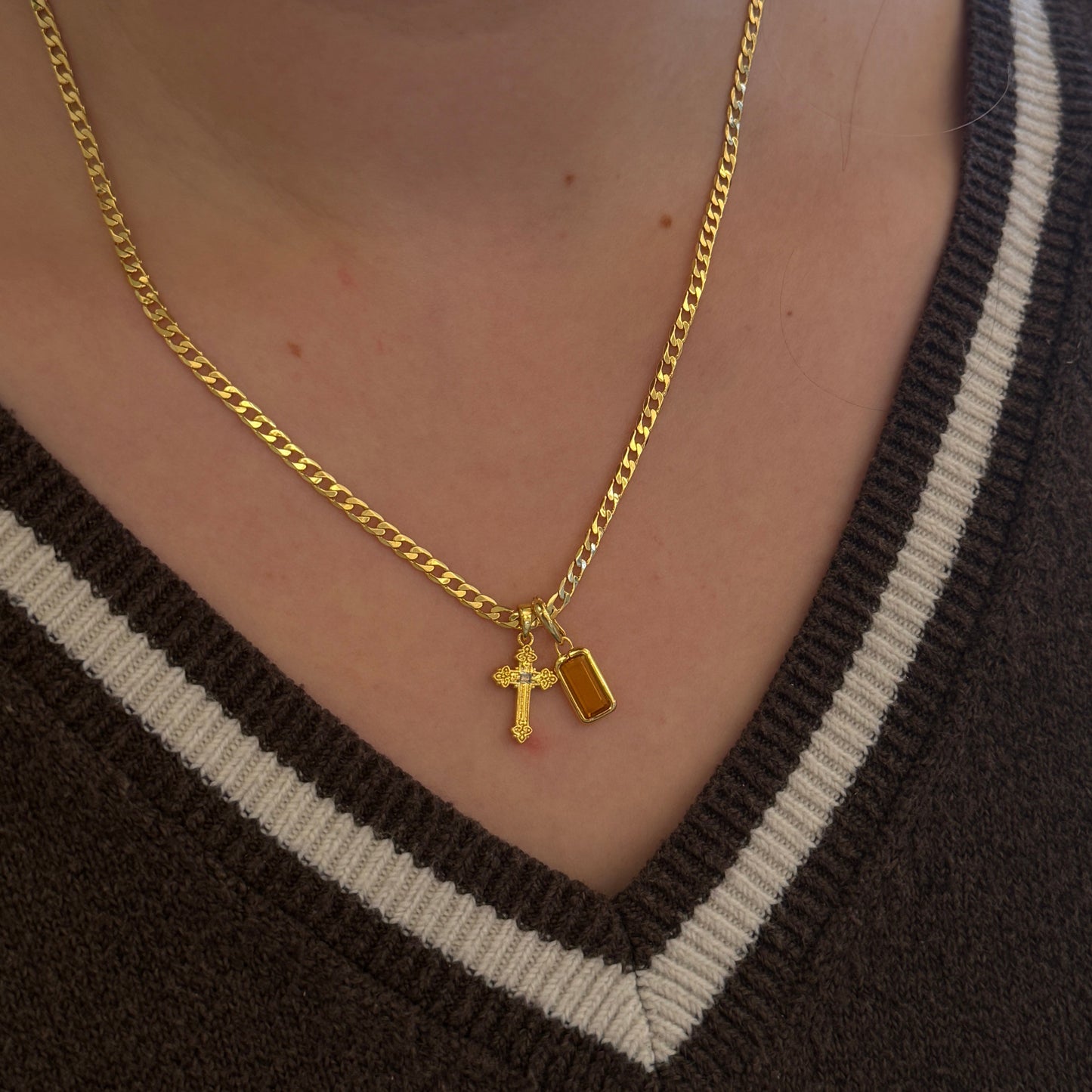 Gold necklace with a mini gold cross and citrine gemstone pendant on a person's neck with a gold chain.