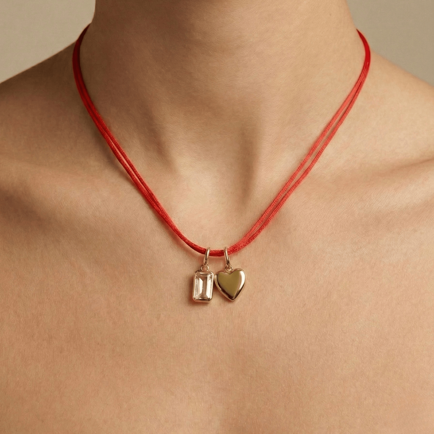 Red necklace with heart and square pendants on a neutral background