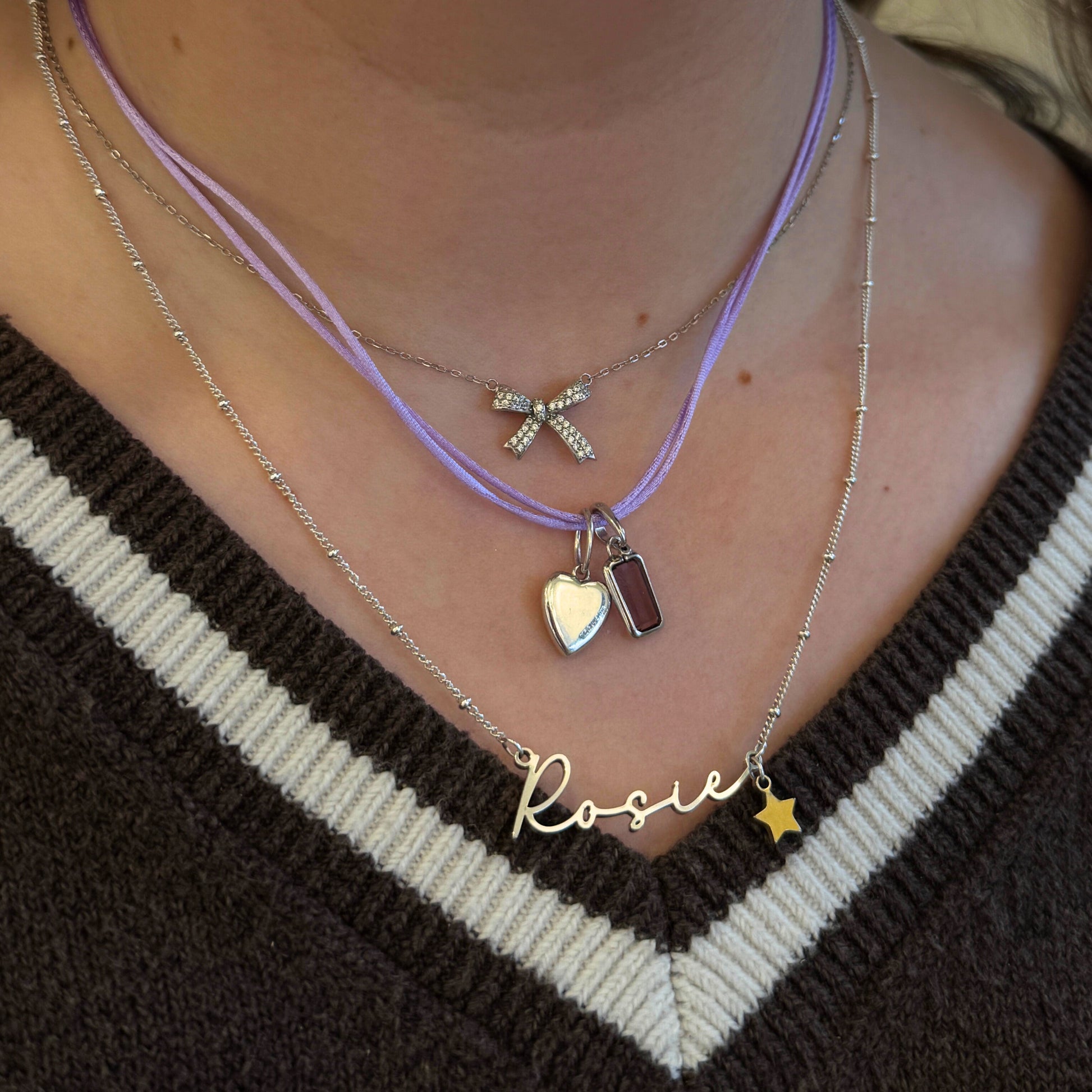 Necklace with various sterling silver pendants including a name charm on a person wearing a brown and white striped sweater.