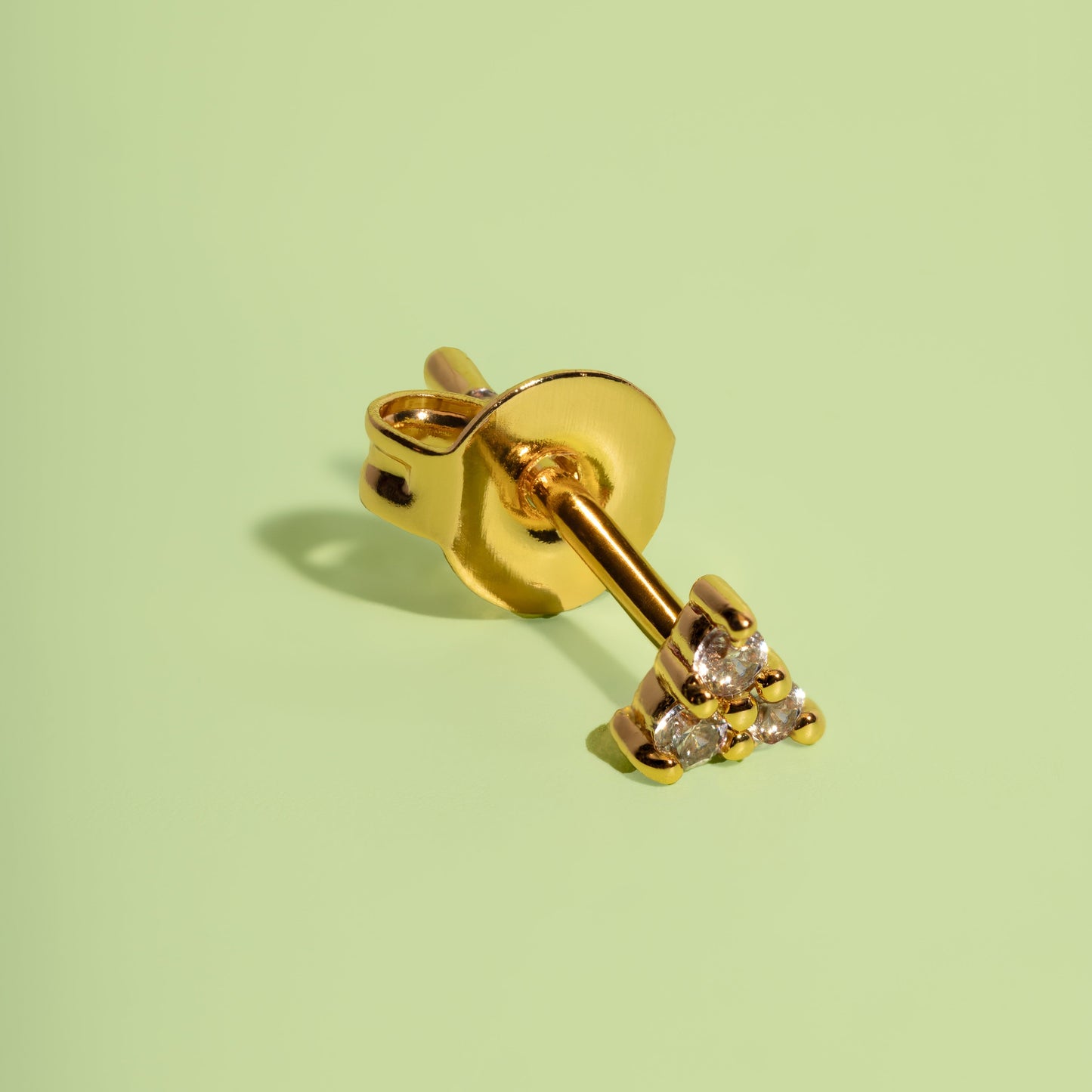 Gold earring with small diamonds on a light green background