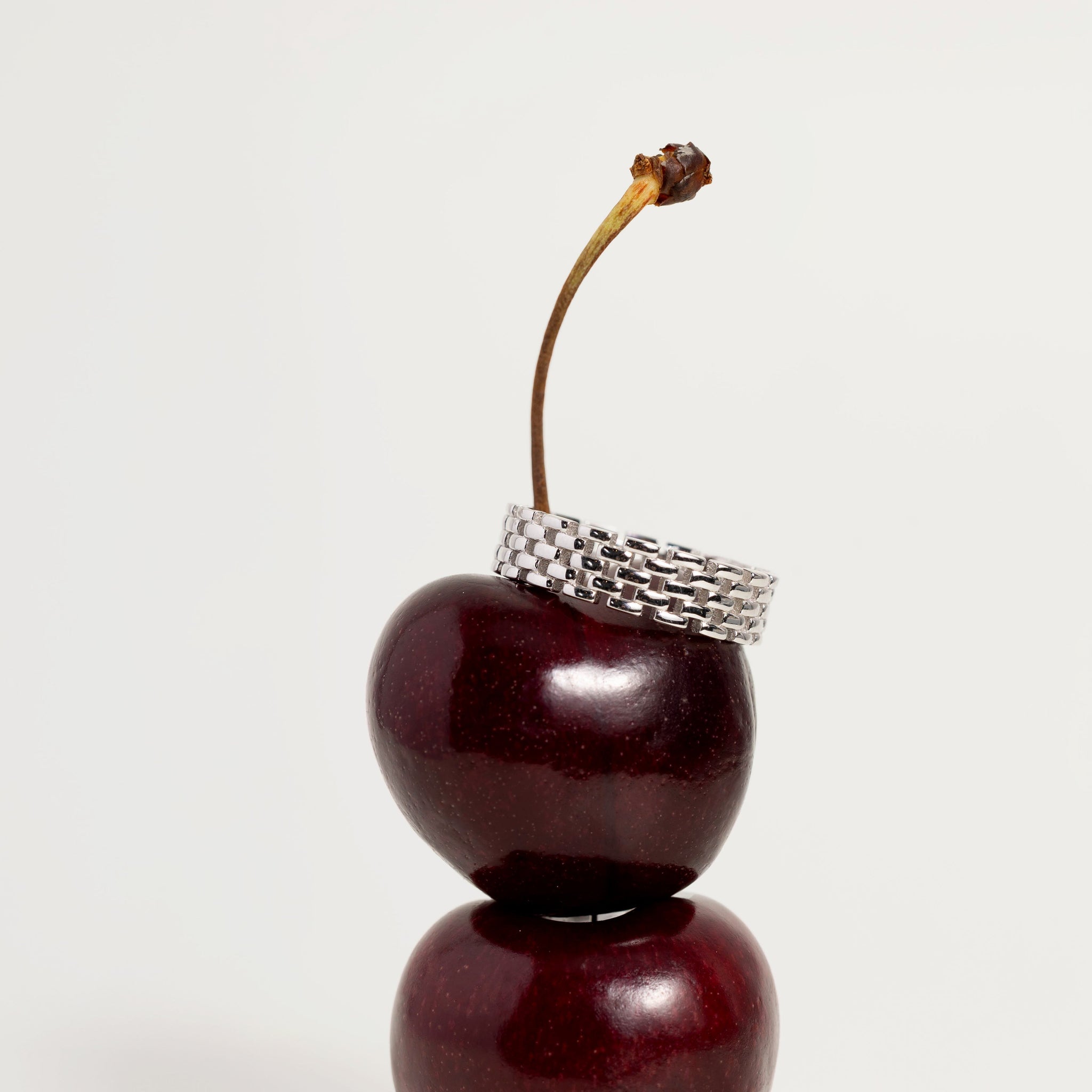 Decorative item resembling a cherry with a silver ring on a white background