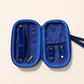 A blue zippered jewelry organizer case shown open, with interior pockets, snap closures, and a wrist strap on a light beige background.