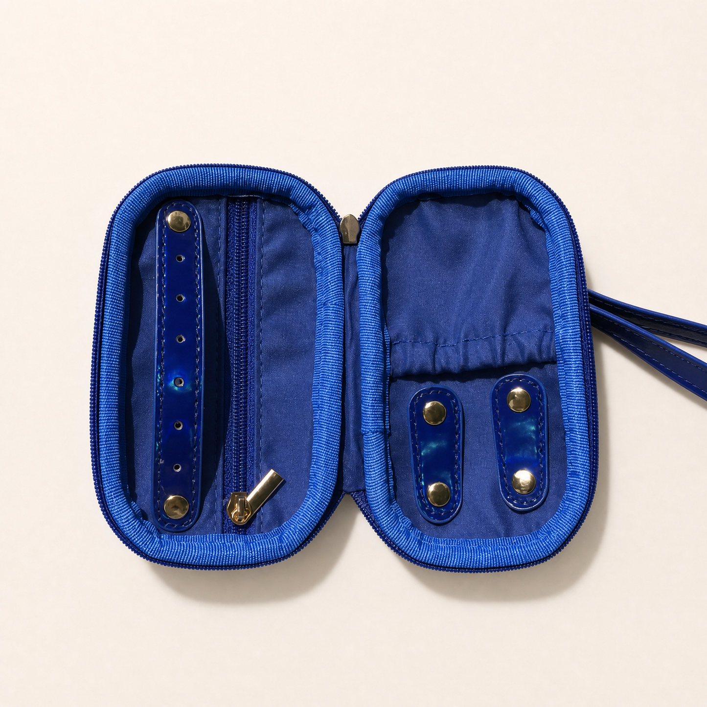 A blue zippered jewelry organizer case shown open, with interior pockets, snap closures, and a wrist strap on a light beige background.