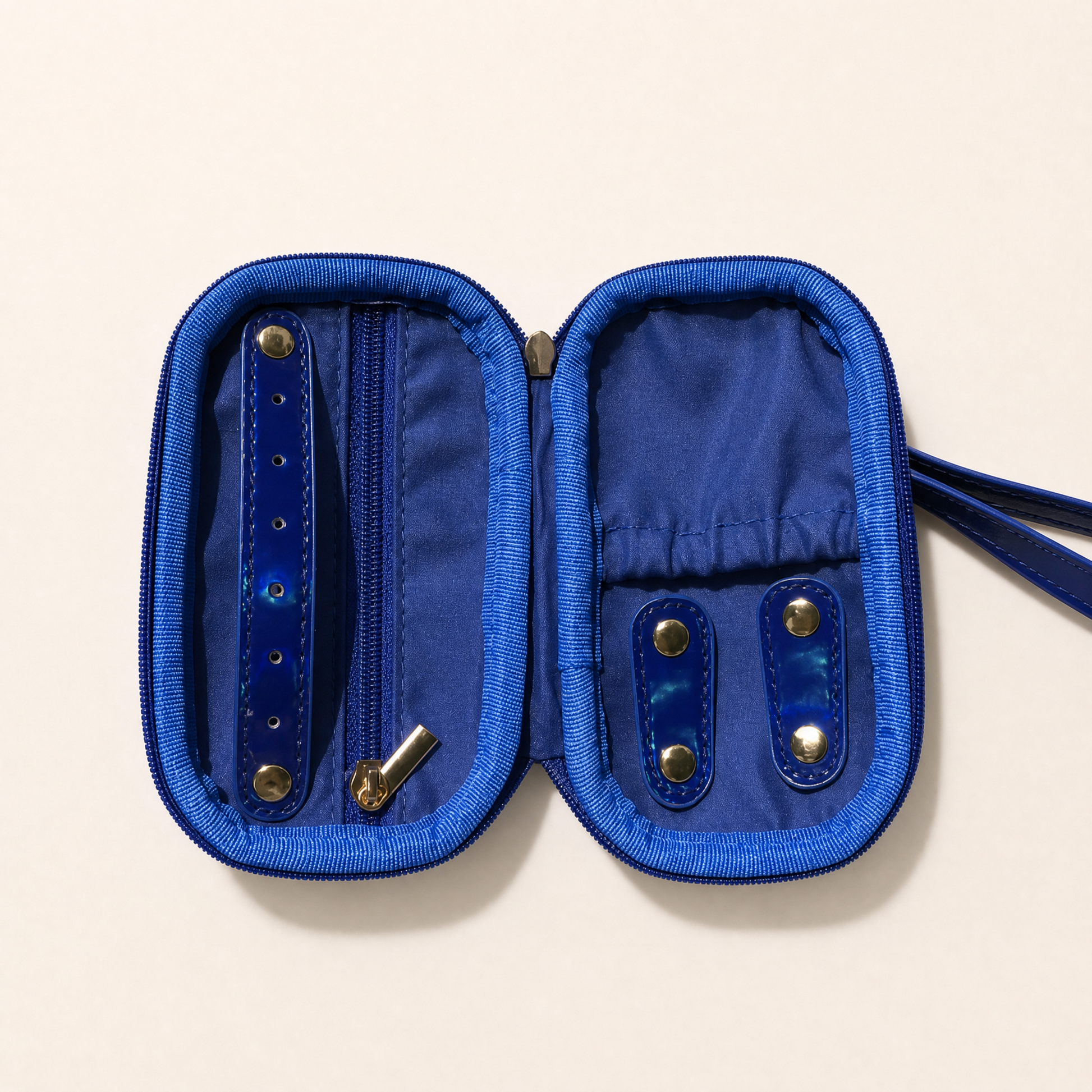 A blue zippered jewelry organizer case shown open, with interior pockets, snap closures, and a wrist strap on a light beige background.