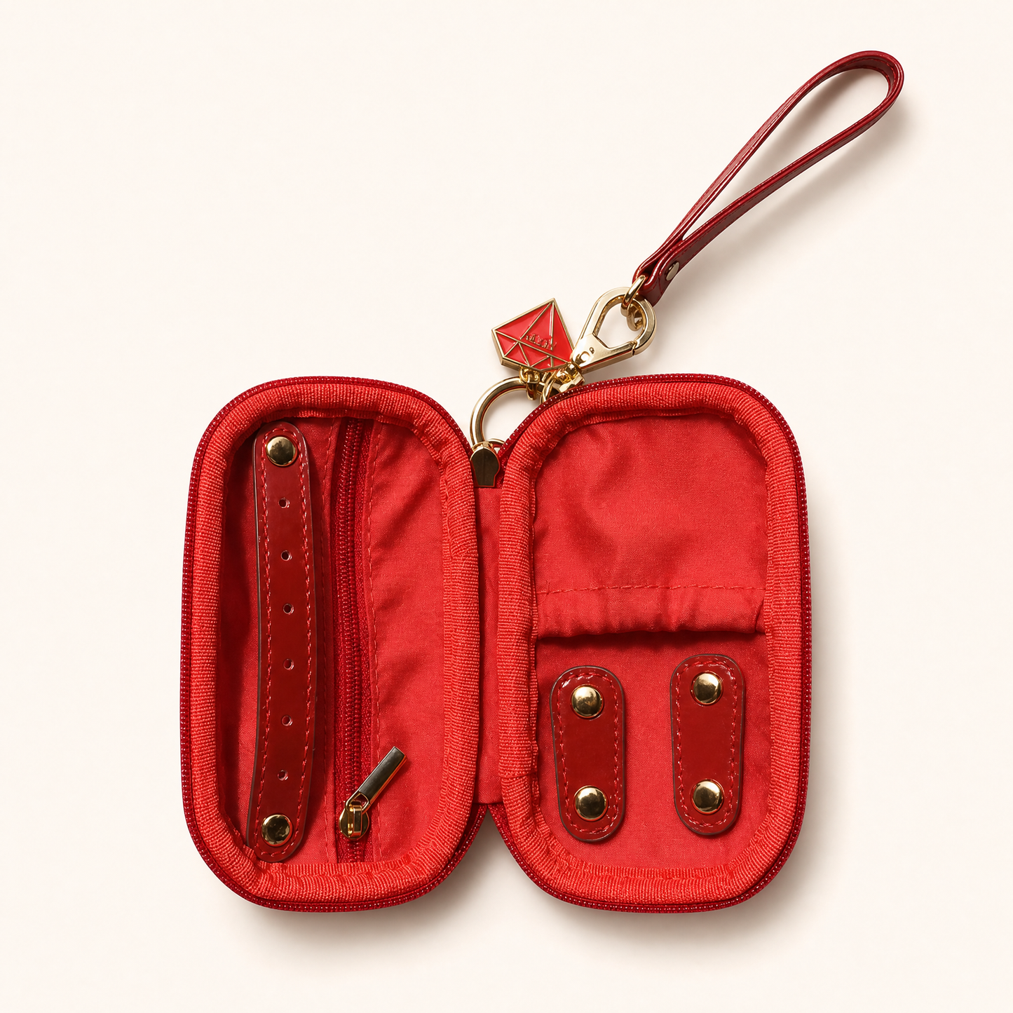 A red fabric and leather jewelry holder shown open, featuring a wrist strap, gold-tone hardware, and internal card slots, photographed on a light cream background.